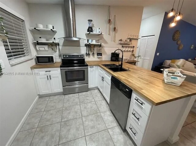 kitchen with appliances with stainless steel finishes, sink, pendant lighting, butcher block countertops, and white cabinetry