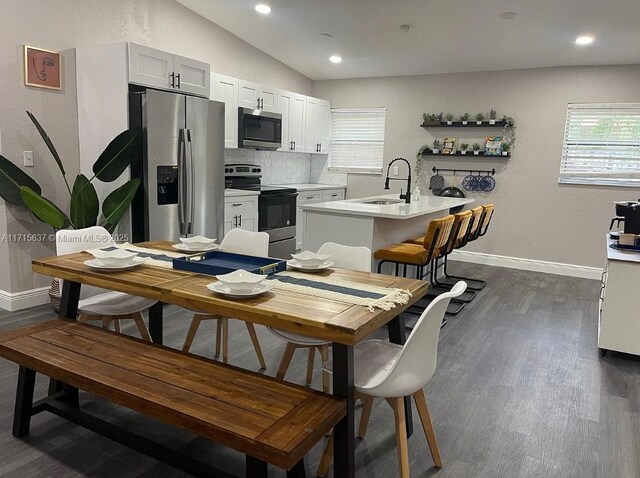 kitchen with white cabinetry, sink, stainless steel appliances, vaulted ceiling, and a center island with sink