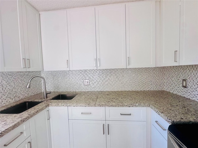 kitchen with tasteful backsplash, white cabinetry, sink, and light stone countertops