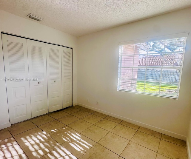 unfurnished bedroom featuring a closet, light tile patterned floors, and a textured ceiling