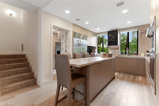 kitchen featuring sink, a breakfast bar area, light hardwood / wood-style floors, a kitchen island, and built in fridge