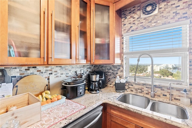 kitchen with tasteful backsplash, light stone counters, stainless steel dishwasher, and sink