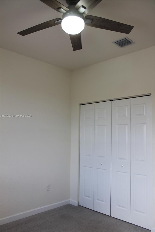 unfurnished bedroom featuring ceiling fan, dark carpet, and a closet