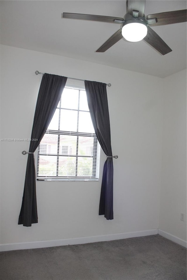 empty room featuring dark colored carpet, ceiling fan, and a wealth of natural light