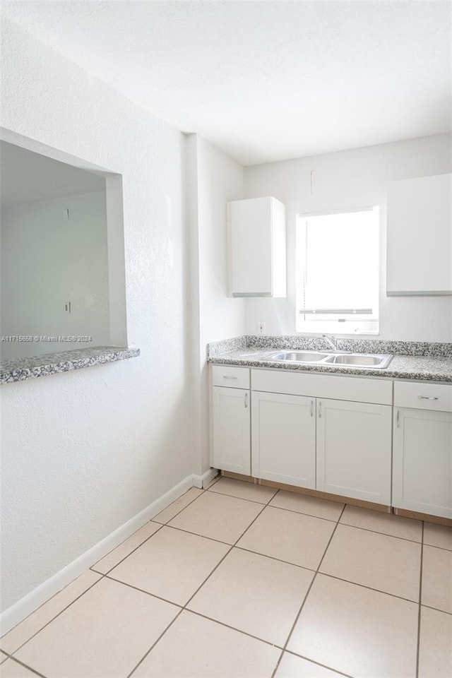 kitchen with white cabinets, light stone counters, light tile patterned floors, and sink