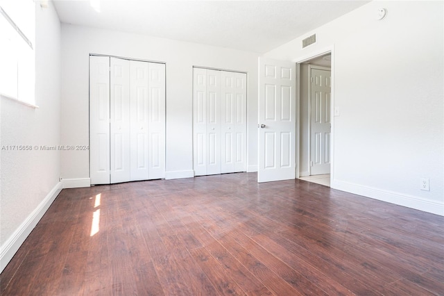 unfurnished bedroom featuring dark hardwood / wood-style floors and two closets