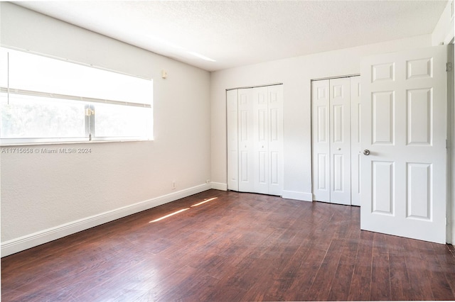 unfurnished bedroom with a textured ceiling, dark wood-type flooring, and two closets