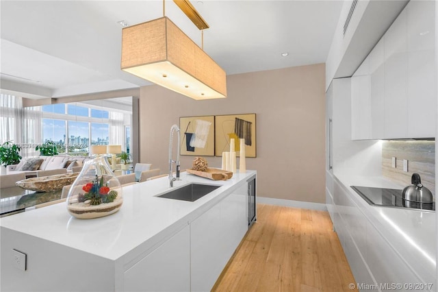 kitchen with sink, white cabinets, a center island with sink, and light hardwood / wood-style flooring