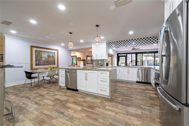 kitchen featuring kitchen peninsula, stainless steel appliances, sink, decorative light fixtures, and white cabinets