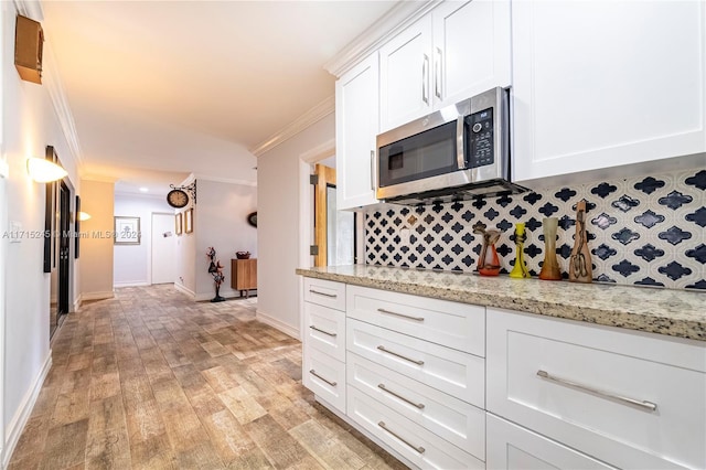 kitchen with light hardwood / wood-style floors, white cabinetry, ornamental molding, and light stone counters