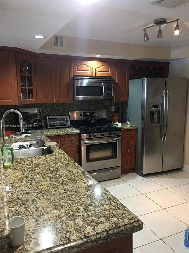 kitchen with tasteful backsplash, stainless steel appliances, sink, light tile patterned floors, and stone counters