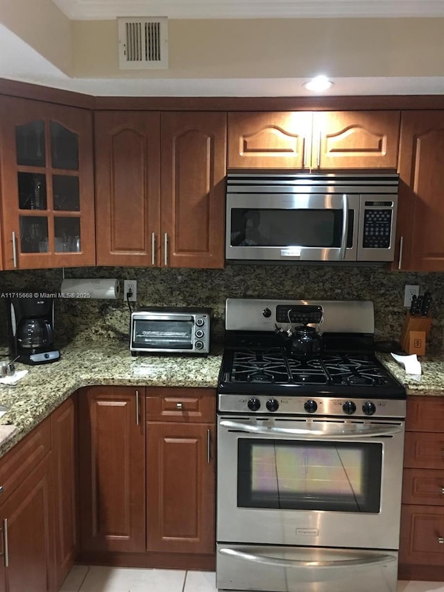 kitchen featuring a toaster, visible vents, appliances with stainless steel finishes, glass insert cabinets, and light stone countertops