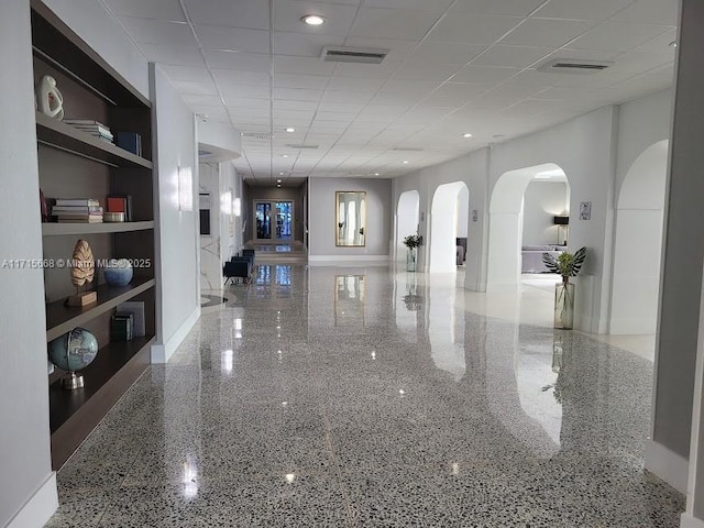 hallway with arched walkways, a drop ceiling, visible vents, and speckled floor