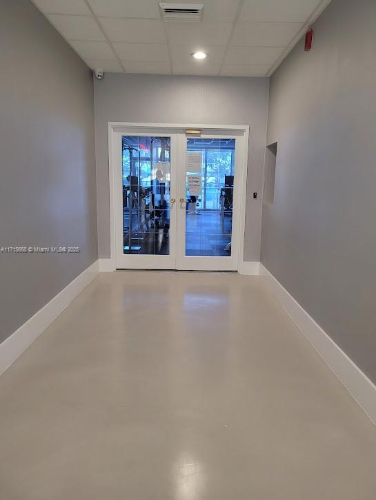 spare room with finished concrete flooring, baseboards, a drop ceiling, and french doors