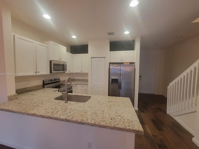 kitchen with kitchen peninsula, sink, appliances with stainless steel finishes, light stone counters, and white cabinetry