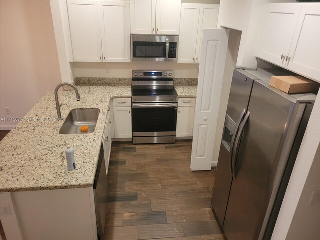 kitchen with light stone counters, stainless steel appliances, dark wood-type flooring, sink, and white cabinetry