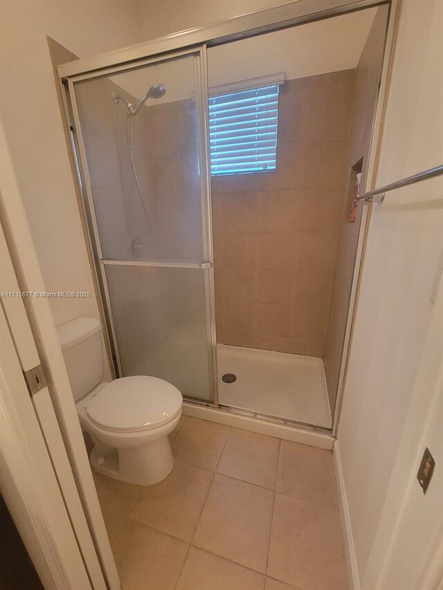 bathroom with tile patterned floors, a shower with door, and toilet