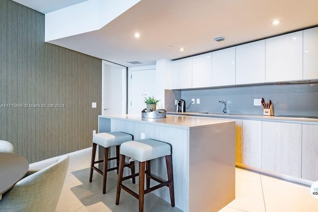 kitchen featuring a kitchen breakfast bar, sink, white cabinets, a center island, and light tile patterned flooring