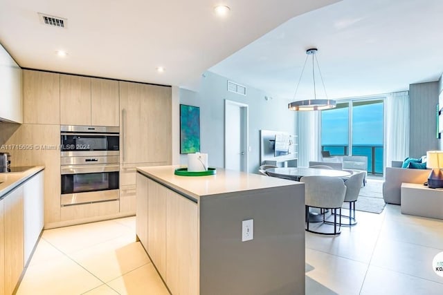 kitchen with light brown cabinets, a center island, decorative light fixtures, and double oven