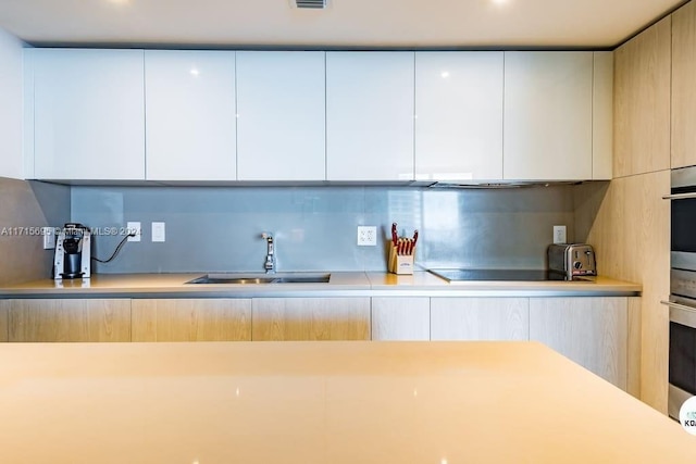 kitchen with tasteful backsplash, white cabinetry, sink, and black electric stovetop