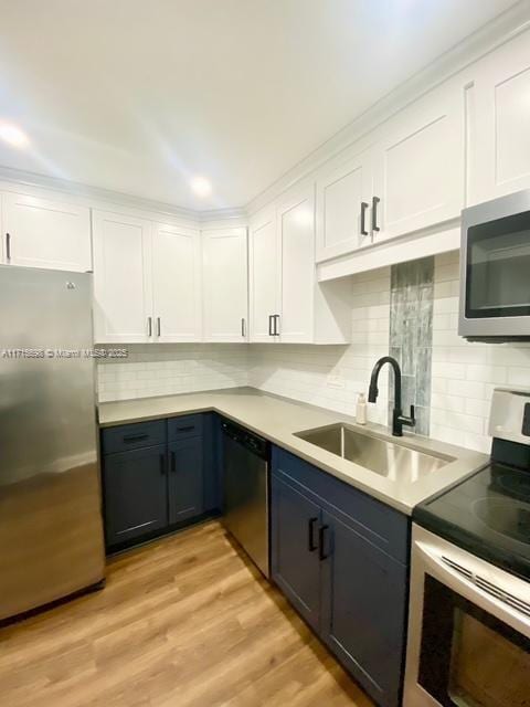 kitchen with sink, white cabinetry, stainless steel appliances, decorative backsplash, and light wood-type flooring