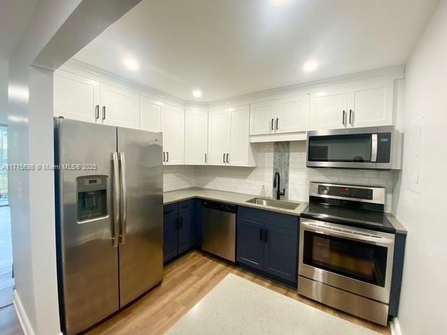 kitchen featuring blue cabinetry, sink, white cabinetry, light hardwood / wood-style flooring, and appliances with stainless steel finishes