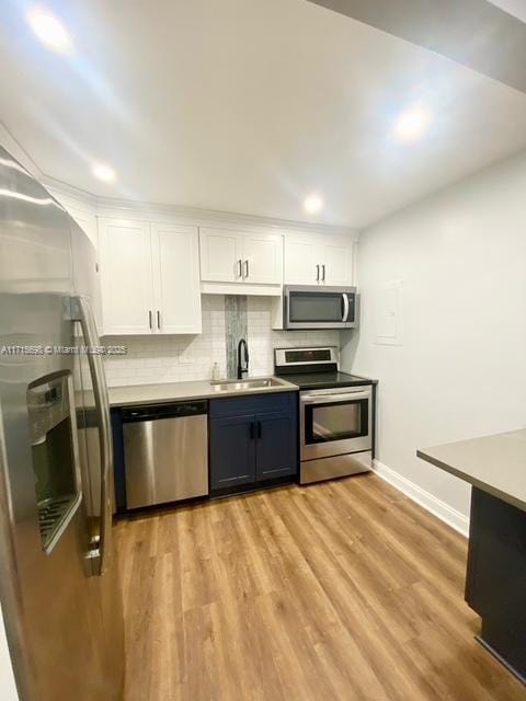 kitchen with sink, white cabinetry, light hardwood / wood-style flooring, stainless steel appliances, and backsplash