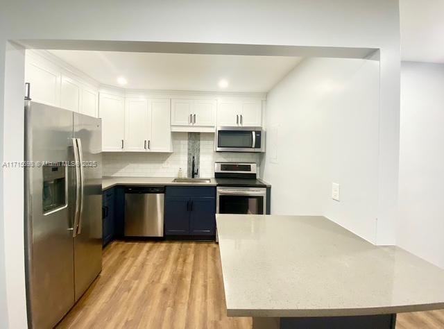 kitchen with blue cabinetry, sink, white cabinetry, appliances with stainless steel finishes, and backsplash