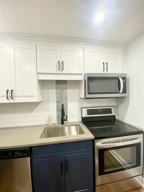 kitchen featuring appliances with stainless steel finishes, blue cabinets, white cabinetry, sink, and backsplash