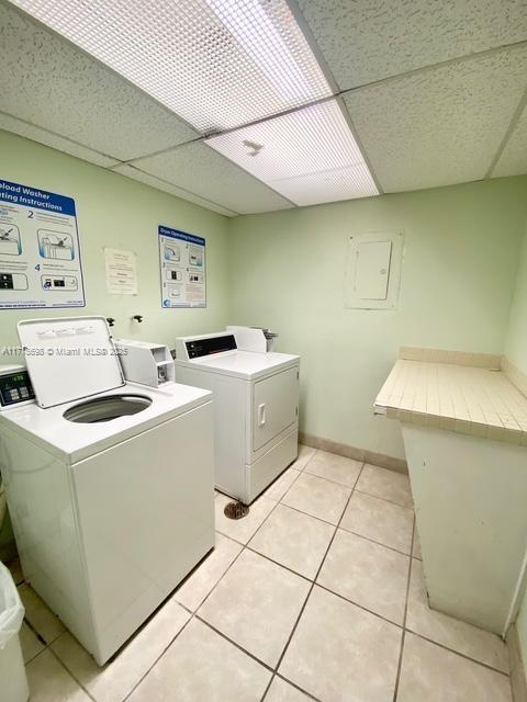 laundry area featuring electric panel, washer and dryer, and light tile patterned flooring