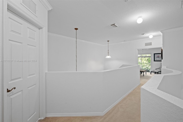 hallway with a textured ceiling, ornamental molding, and light carpet