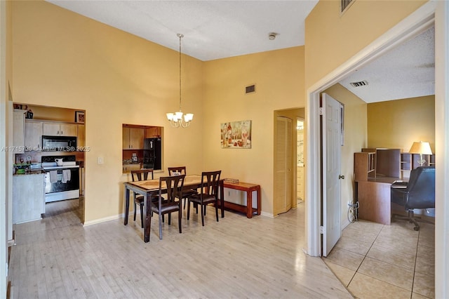 dining area featuring a high ceiling, a textured ceiling, light hardwood / wood-style floors, and an inviting chandelier