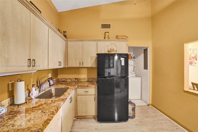 kitchen featuring light stone countertops, black fridge, light hardwood / wood-style floors, sink, and washer / clothes dryer