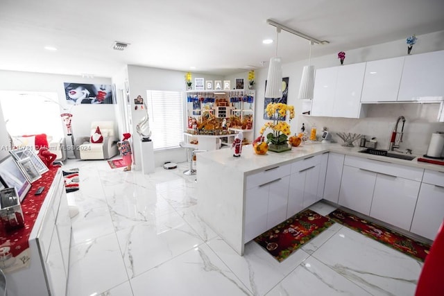 kitchen featuring sink, hanging light fixtures, kitchen peninsula, decorative backsplash, and white cabinets