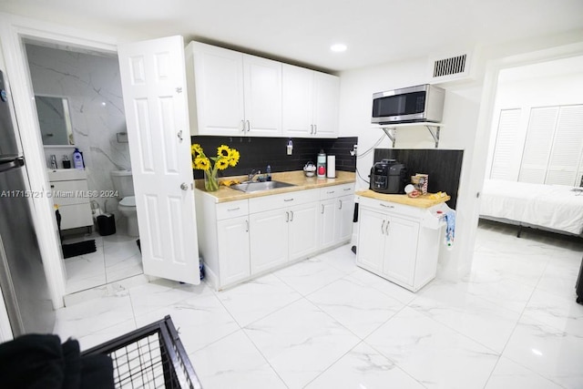 kitchen with backsplash, white cabinetry, and sink