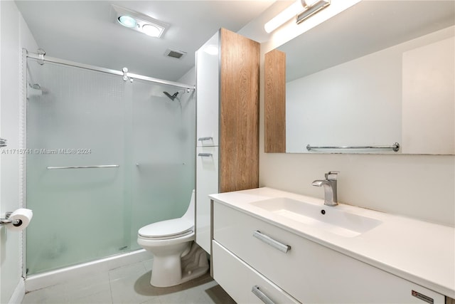 bathroom featuring tile patterned flooring, vanity, toilet, and a shower with shower door