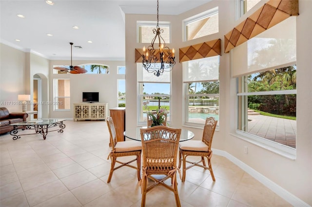 dining area featuring ceiling fan with notable chandelier, light tile patterned flooring, ornamental molding, and a high ceiling