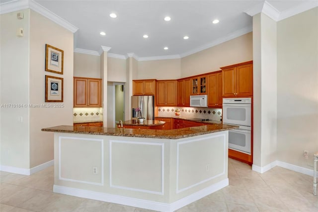 kitchen with white appliances, backsplash, a large island with sink, dark stone counters, and light tile patterned floors