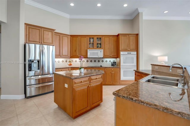 kitchen with ornamental molding, dark stone counters, white appliances, a kitchen island with sink, and sink