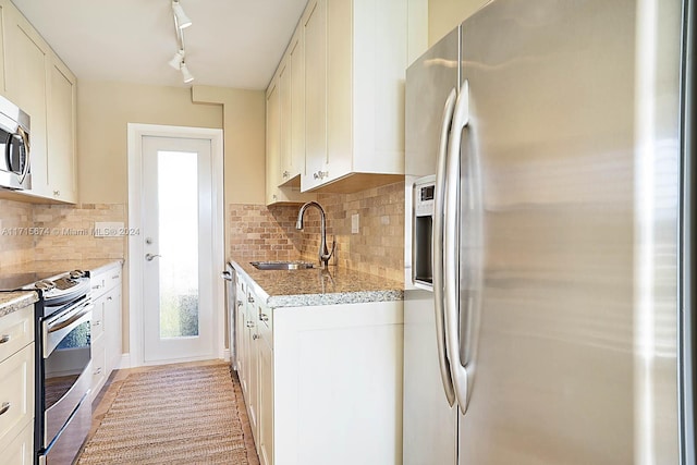 kitchen featuring sink, rail lighting, stainless steel appliances, tasteful backsplash, and white cabinets