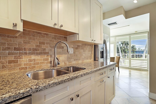 kitchen featuring tasteful backsplash, light stone counters, sink, and white cabinets