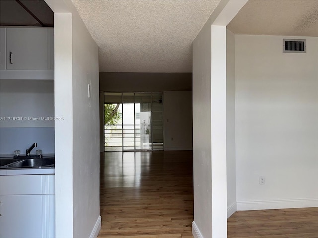 hall with a sink, visible vents, a textured ceiling, and light wood-style flooring