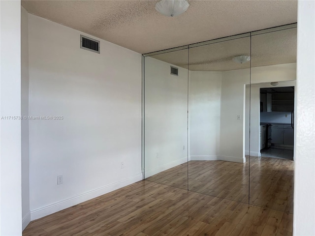 unfurnished room with wood finished floors, visible vents, and a textured ceiling