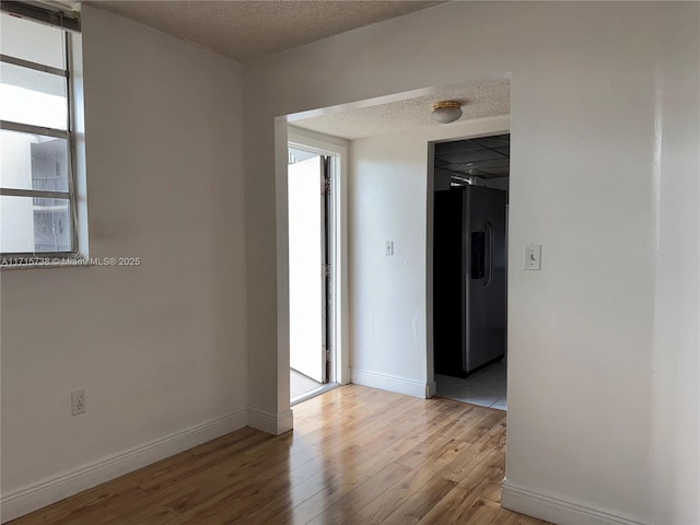 spare room featuring light wood finished floors, a textured ceiling, and baseboards