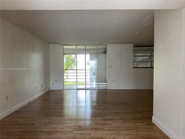 spare room with a wall of windows, baseboards, and wood finished floors