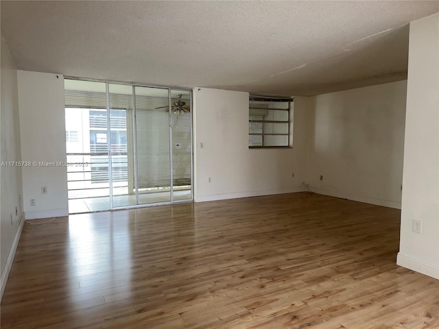 spare room with ceiling fan, baseboards, expansive windows, wood finished floors, and a textured ceiling