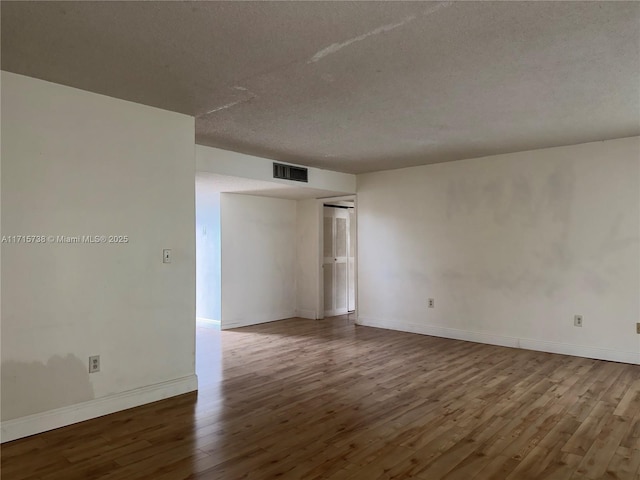 empty room featuring a textured ceiling, wood finished floors, visible vents, and baseboards