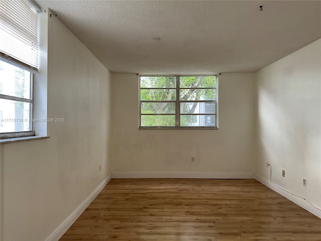 spare room with baseboards, light wood-style floors, and a textured ceiling