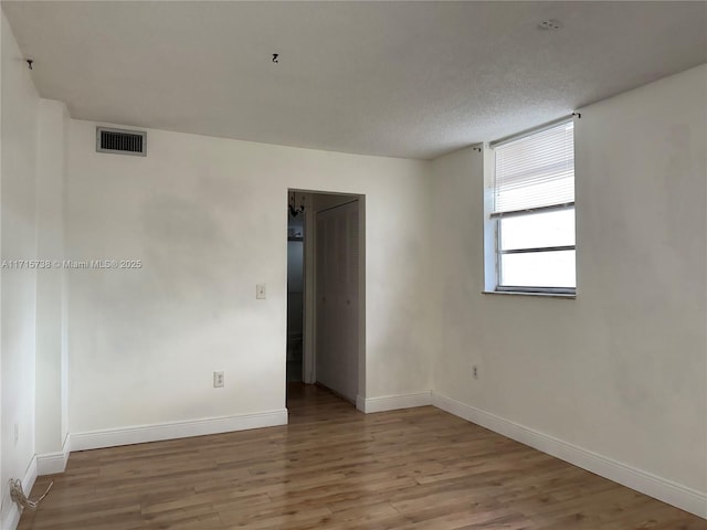 spare room with visible vents, baseboards, a textured ceiling, and wood finished floors