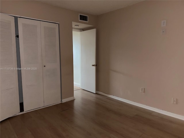 unfurnished bedroom featuring wood finished floors, visible vents, a closet, and baseboards